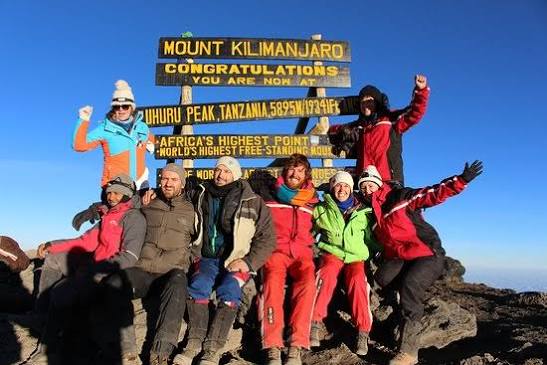 Successful travelers standing triumphant on the Roof of Africa at sunrise